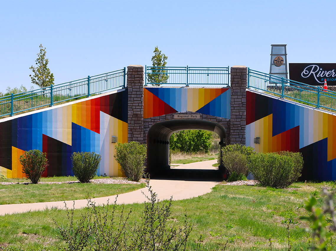 Colorful mural on pedestrian underpass with "Regional Park" sign, surrounded by greenery, blue sky above