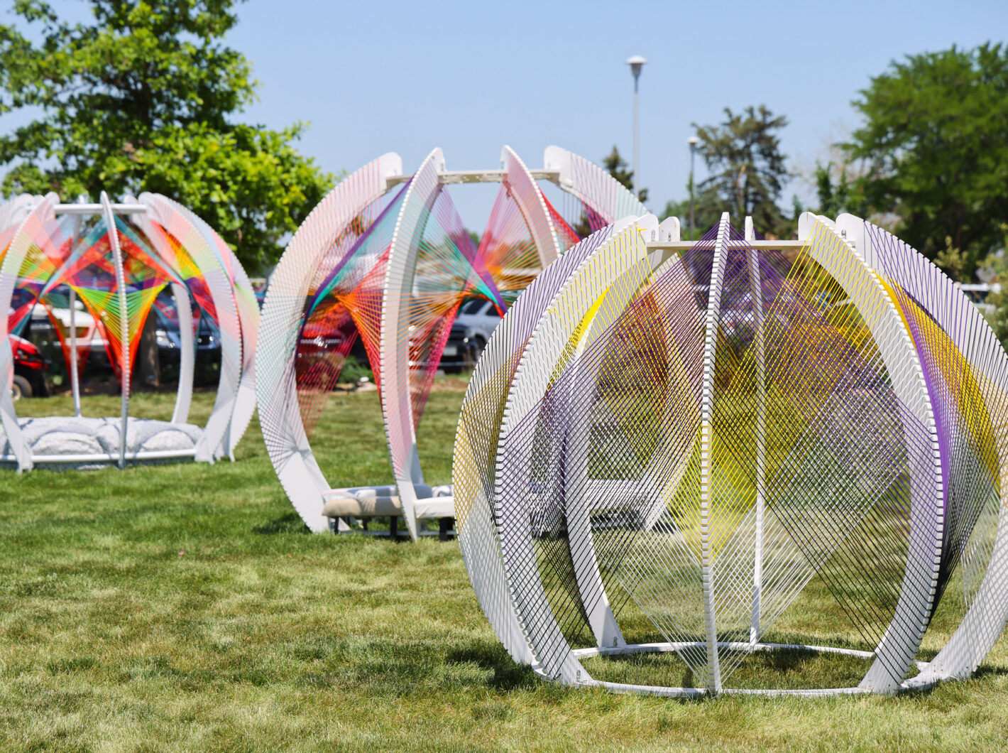 Colorful geometric installations with strings on a grassy field, bright day