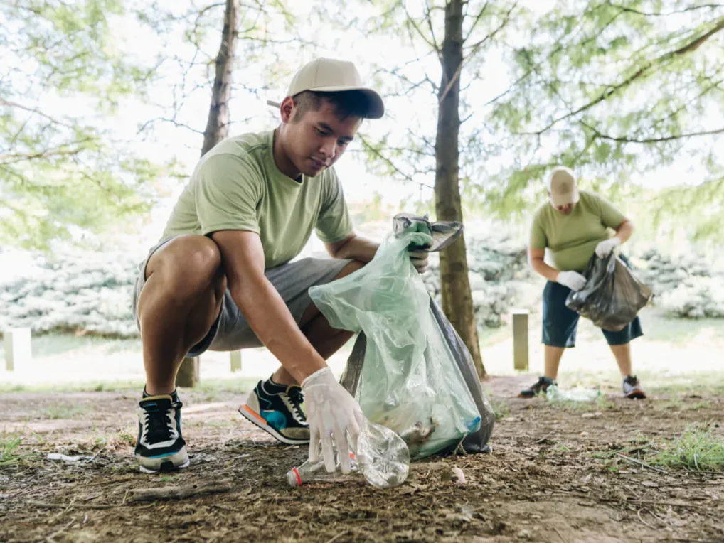 Two people picking up litter in a park, wearing green shirts and gloves