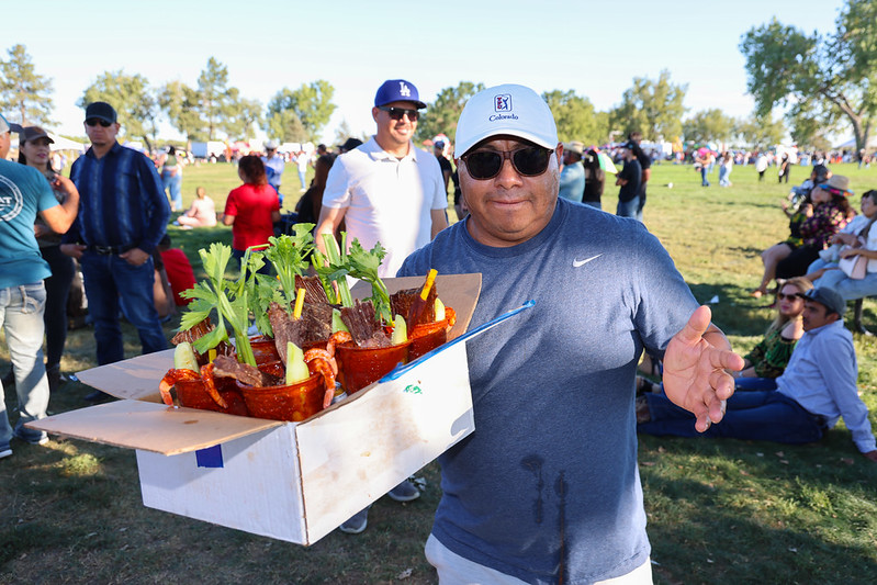 Man carrying a tray of drinks with garnishes at an outdoor gathering