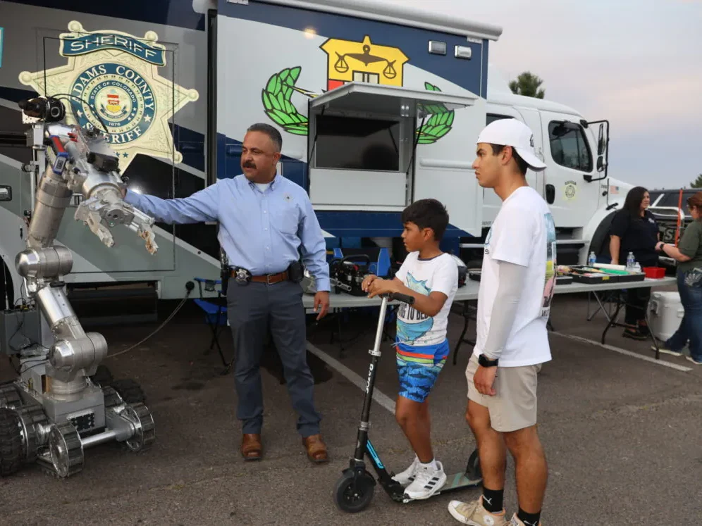 Man demonstrating robot to two boys on scooters at a fair