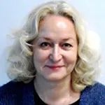 Alena smiling with curly blonde hair, wearing a blue sweater