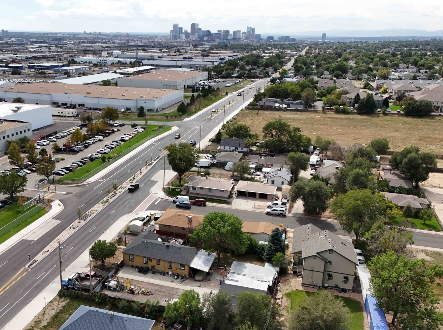 Aerial view of a suburban neighborhood with distant city skyline, roads, and industrial buildings