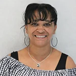 Najla Najee-Ulla smiling, wearing hoop earrings and a plaid top