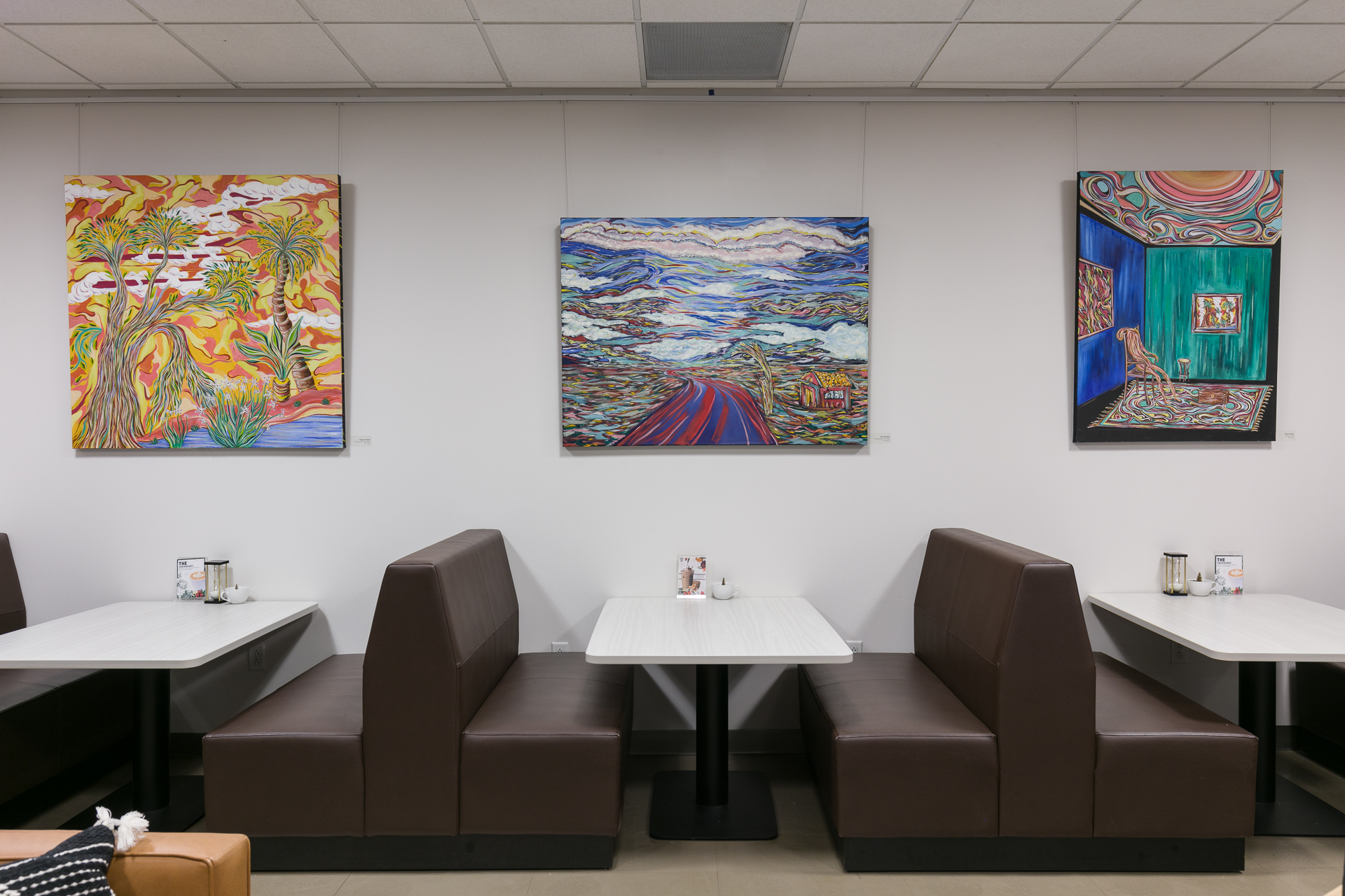 Art gallery with colorful abstract paintings above brown leather booths