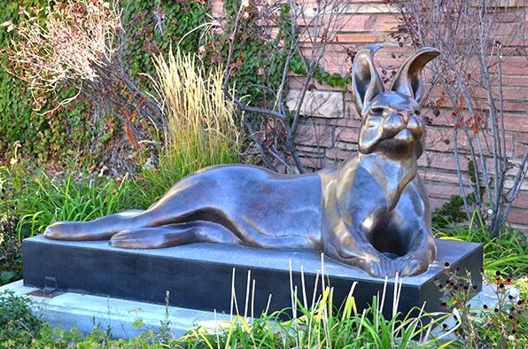 Bronze jackalope sculpture in a garden setting with brick wall