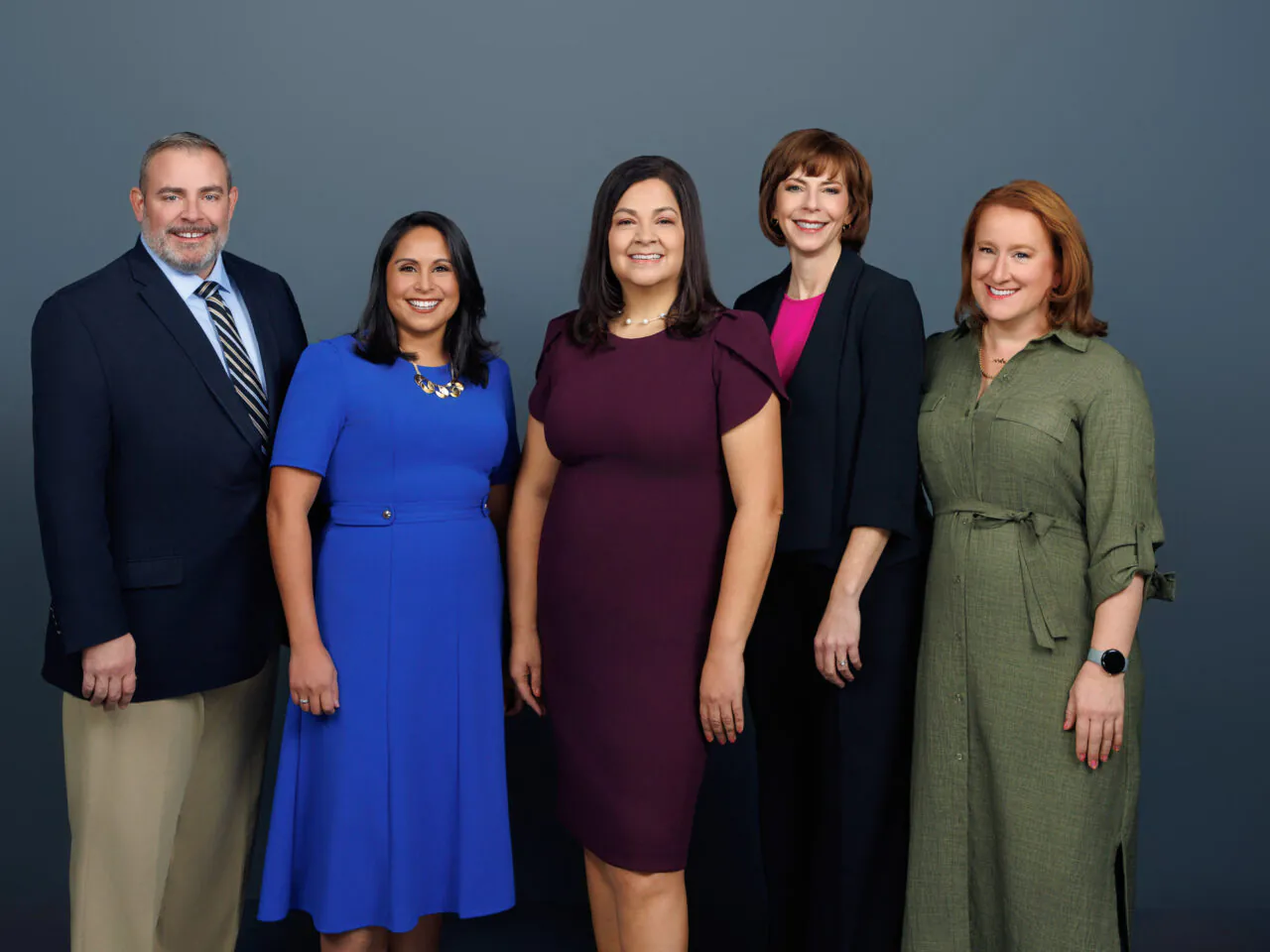 Group of five smiling individuals in professional attire against a gray background