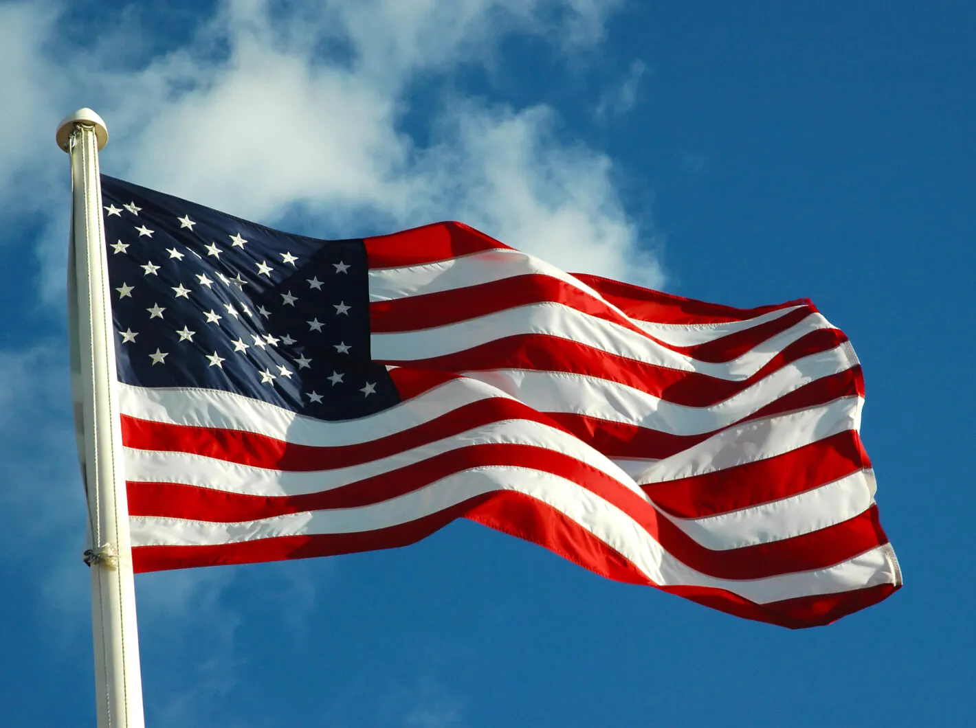 American flag waving against a blue sky with clouds