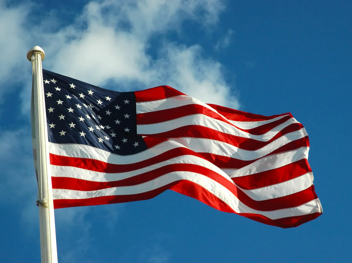 American flag waving against a blue sky with clouds