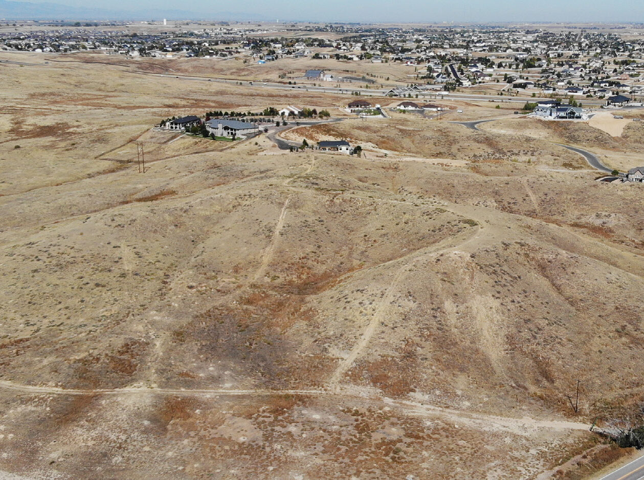 Aerial view of Riverdale Bluffs, showing dry, hilly terrain with a distant residential neighborhood